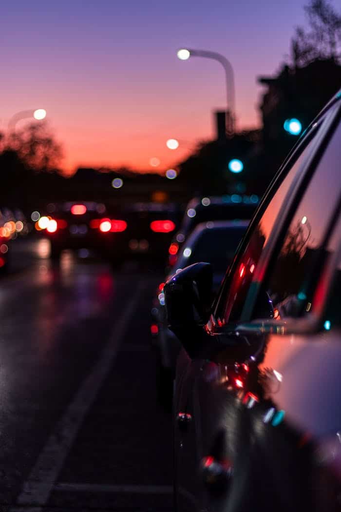 Blurred city street scene at dusk with vibrant lights reflecting on car surface, capturing nightlife essence.