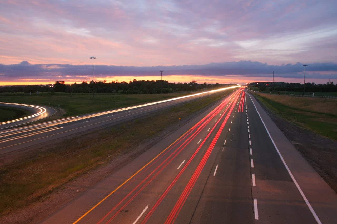 Long exposure highway shot showcasing vibrant car light trails against a sunset sky.